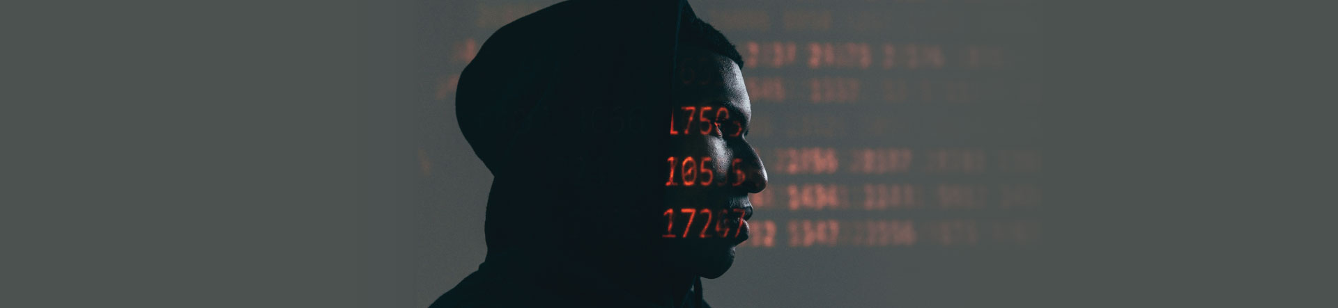 Silhoutte of a suspicious looking man with code projected on to his face to illustrate the need for Cybercrime Defence