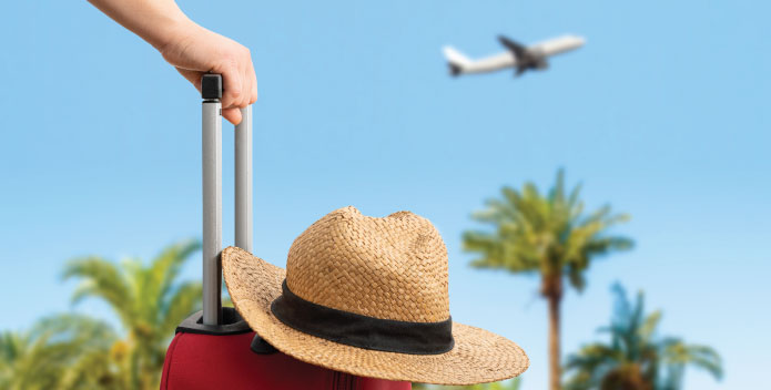 Suitcase with a straw hat resting on top with palm trees and a holiday jet taking off in a clear blue sky - travel tech for holidays